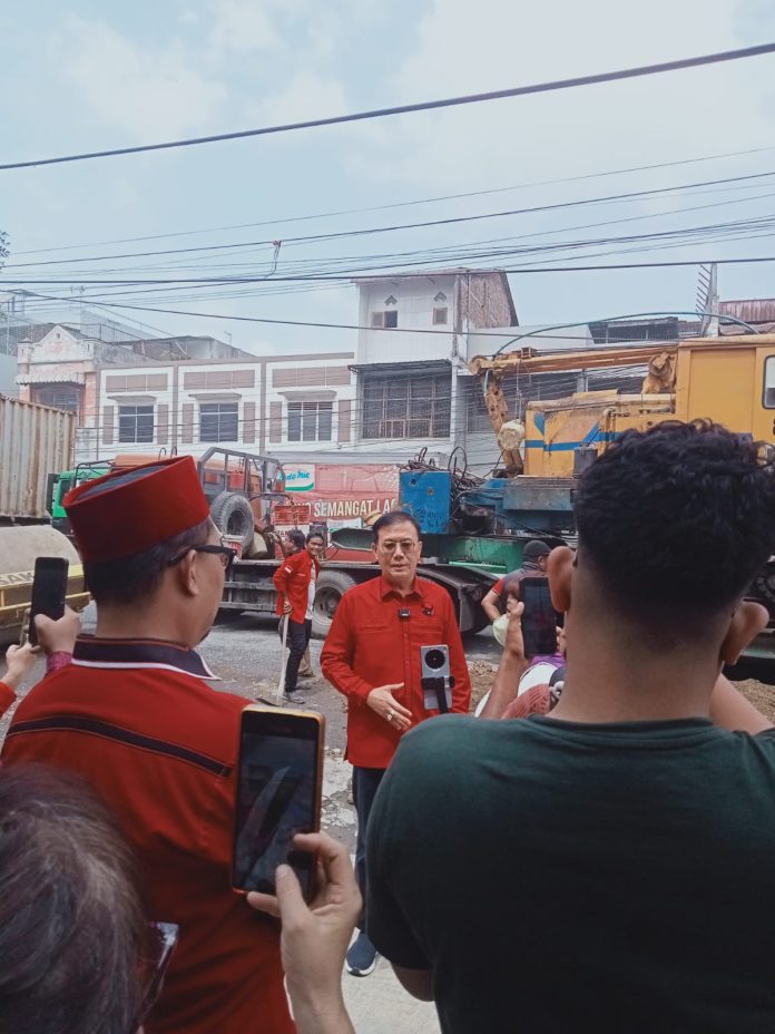 IMG-20261009-WA0071 Teks Foto : Hasyim, SE saat diwawancarai wartawan, Jumat (09/10/2026) saat meninjau penimbunan jalan di ruas Jln. KL Yos Sudarso mulai dari Simpang Dobi sampai Simpang Titipapan. Tampak mobil truk kontainer lalu lalang di sepanjang jalan tersebut. (Ist)